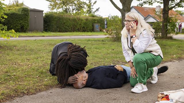 A man performing CPR and a woman calling emergency services