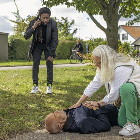 Kvinde som tilser en mand, der er faldet om og en anden person der ringer 112