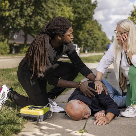To personer som tilser en mand, der er faldet om med en hjertestarter ved siden af som er klar til brug